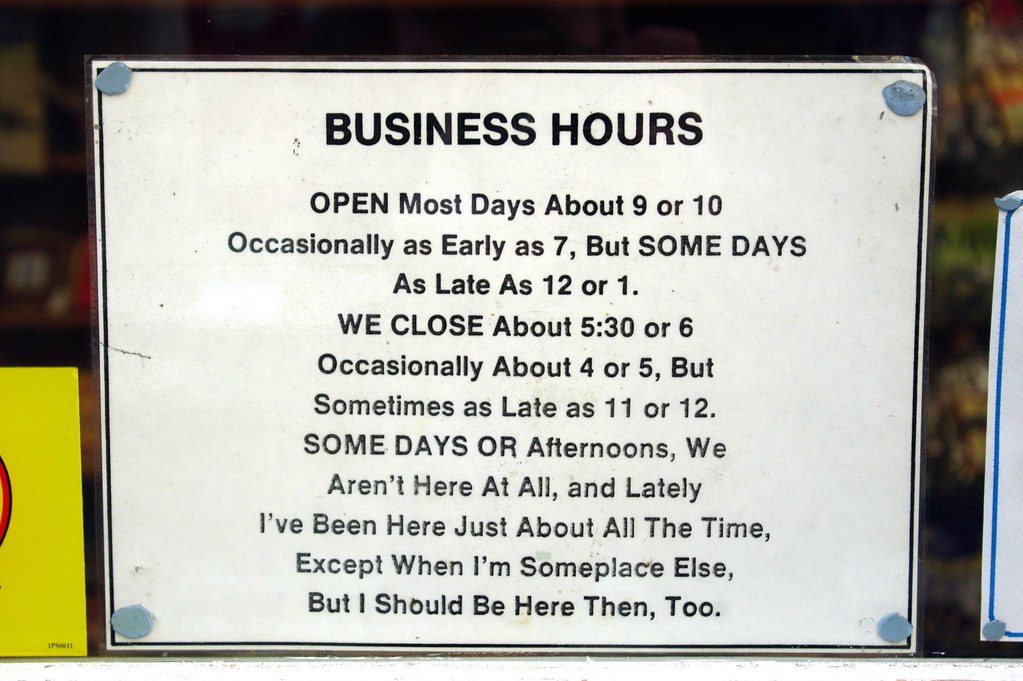 A handwritten business hours sign posted in a shop window listing opening and closing times