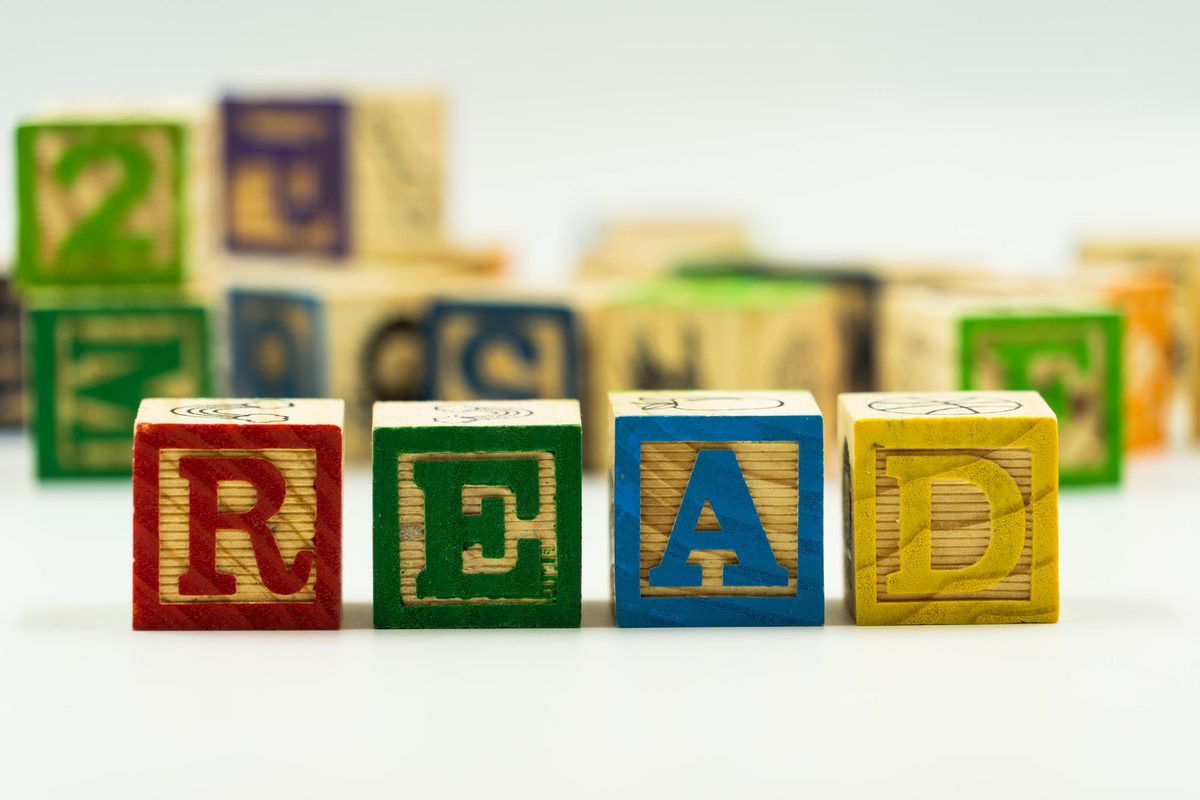 Wooden alphabet blocks spelling the word READ, with more stacked blocks blurred in the background