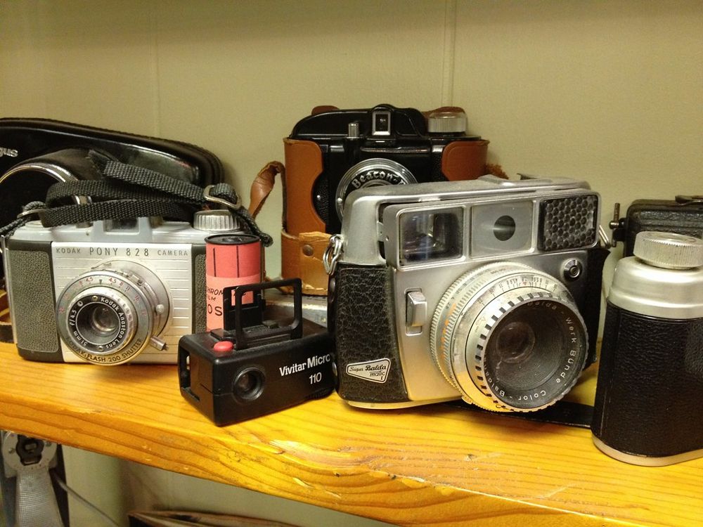 A shelf holding several vintage film cameras, including a Kodak Pony 828 and a Super Balda camera