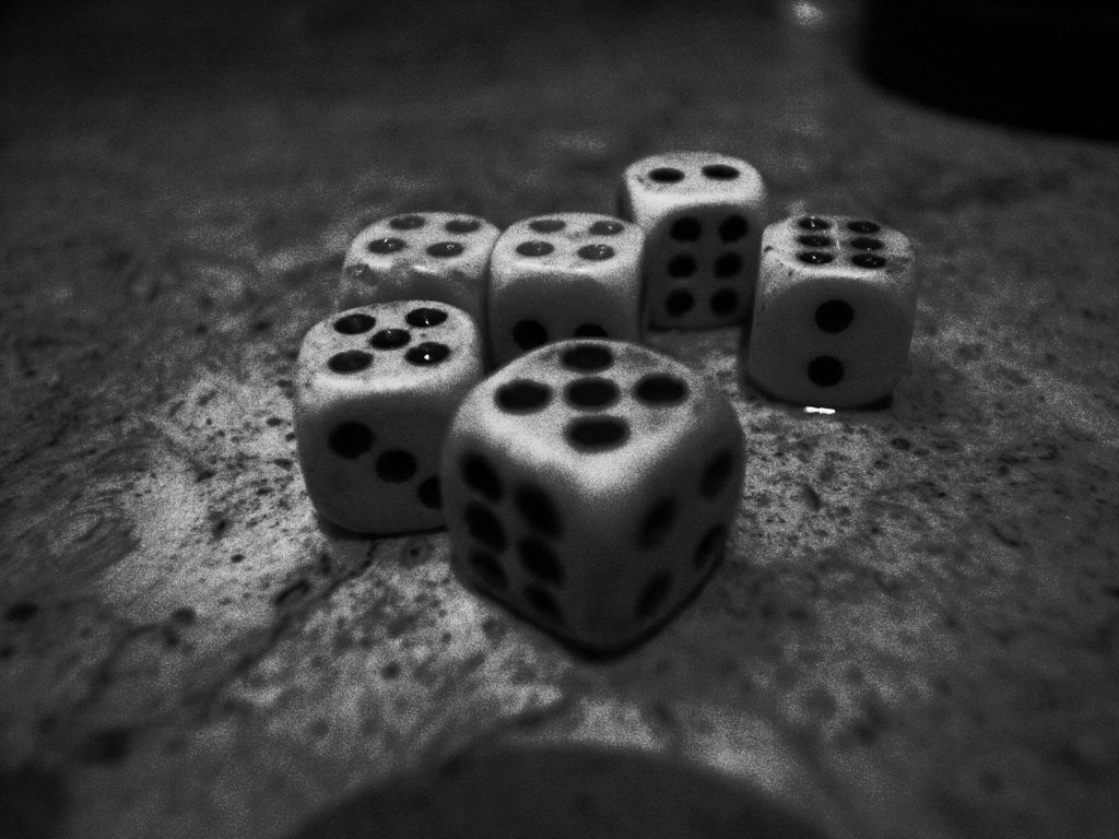 Six white dice with black pips scattered on a table in black and white, each showing a different number